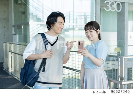 大学の通路でスマホを見ながら話をする大学生の男女 大学の通路でスマホを見ながら話をする大学生の男女 96627340