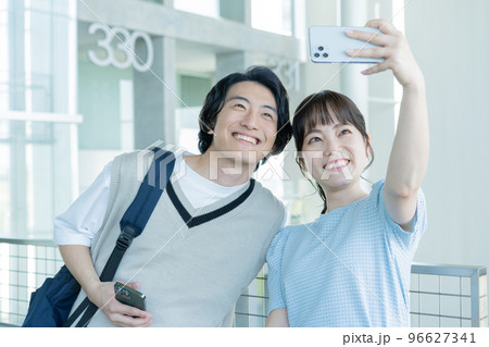 大学の通路でスマホで写真を撮る大学生の男女 96627341