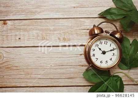 Alarm clock with green leave border frame on wooden background 96628145