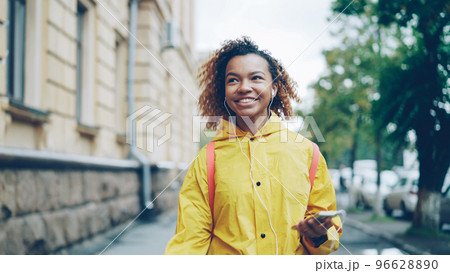 Carefree African American student is walking, listening to music through earphones during leisure time. Modern technology, youth culture, cities and people concept. Carefree African American student is walking, listening to music through earphones during leisure time. Modern technology, youth culture, cities and people concept. 96628890