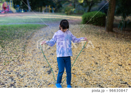 秋の公園で縄跳びをしている小学生の女の子の姿と黄色い銀杏の落ち葉の風景 96630847