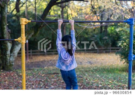 秋の公園で鉄棒を遊んでいる小学生の女の子の姿 96630854