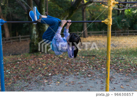 秋の公園で鉄棒を遊んでいる小学生の女の子の姿 96630857