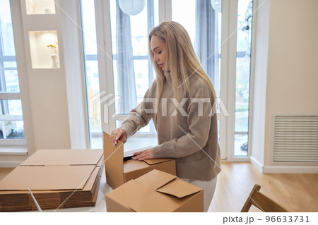 Caucasian girl taping boxes for moving in new apartment. Caucasian girl taping boxes for moving in new apartment. 96633731
