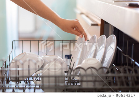 Closeup Shot Of Female Hand Loading Dishes To Dishwasher Machine In Kitchen 96634217