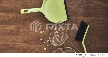 A close-up view from above of a split transparent cup with soup and brushes with a dustpan for cleaning. The concept of home cleaning in the apartment. High quality photo 96634249