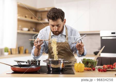 Serious handsome mature caucasian man with beard in apron prepare pasta in minimalist kitchen interior 96634250