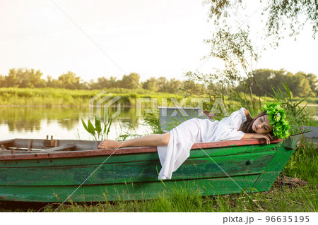 The nymph with long dark hair in a white vintage dress sitting in a boat in the middle of the river. The nymph with long dark hair in a white vintage dress sitting in a boat in the middle of the river. 96635195