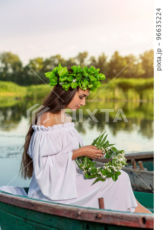 The nymph with long dark hair in a white vintage dress sitting in a boat in the middle of the river. The nymph with long dark hair in a white vintage dress sitting in a boat in the middle of the river. 96635224