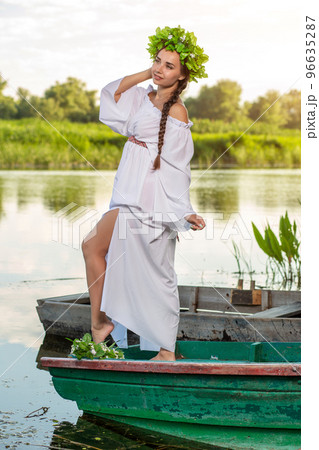 Young sexy woman on boat at sunset. The girl has a flower wreath on her head, relaxing and sailing on river. Fantasy art photography. 96635287