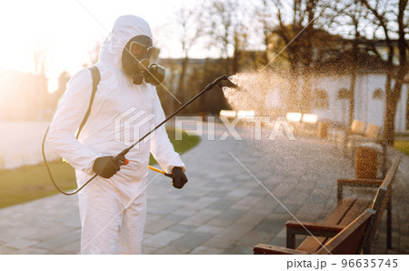 Man wearing protective suit disinfecting public places in the sun with spray chemicals. Covid -19. Man wearing protective suit disinfecting public places in the sun with spray chemicals. Covid -19. 96635745