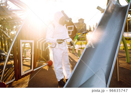 Man wearing protective suit disinfecting the playground in the sun with spray. Covid -19. Cleaning. 96635747