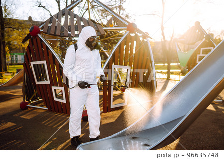 Man wearing protective suit disinfecting the playground in the sun with spray. Covid -19. Cleaning. 96635748
