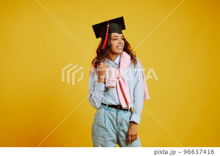 Graduate woman in a graduation hat on her head posing on a yellow background. Study, education, university, college, graduate concept. 96637416
