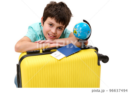 Close-up portrait of a happy teenage boy passenger with yellow suitcase and globe, cutely smiles looking at camera, isolated over white background. Travel. Tourism. Journey concept Free ad space Close-up portrait of a happy teenage boy passenger with yellow suitcase and globe, cutely smiles looking at camera, isolated over white background. Travel. Tourism. Journey concept Free ad space 96637494