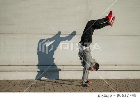 Caucasian man in hooded sweatshirt doing handstand outdoors.  96637749