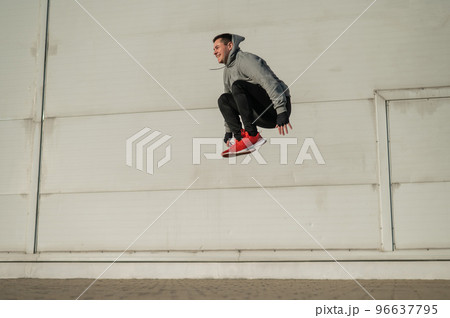 Caucasian man in hoodie jumping high with hands on knees outdoors.  96637795