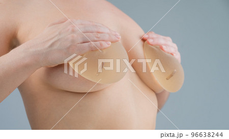 Caucasian naked woman trying on silicone breast implants on a white background. 96638244