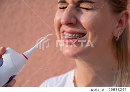 A woman with braces on her teeth uses an irrigator. Close-up portrait.  96638245