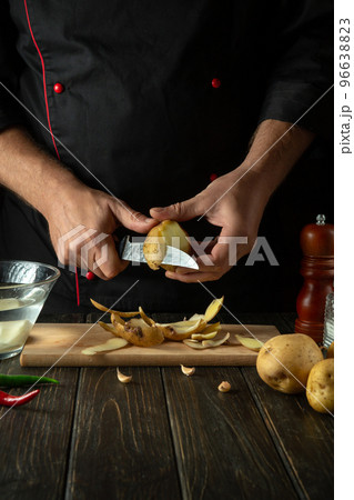 The chef peels potatoes for cooking French fries. Working environment in the kitchen of a restaurant or cafe. The chef peels potatoes for cooking French fries. Working environment in the kitchen of a restaurant or cafe. 96638823