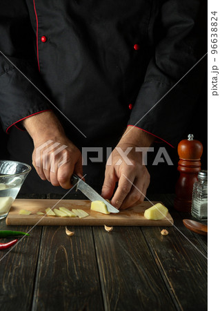 Before preparing the national dish, the chef cuts raw potatoes into small pieces with a knife. Close-up of a cook hands while working in a restaurant kitchen. 96638824