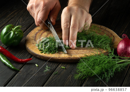 The chef cuts green dill or fennel on a cutting board with a knife for cooking vegetarian food. Peasant food. The chef cuts green dill or fennel on a cutting board with a knife for cooking vegetarian food. Peasant food. 96638857