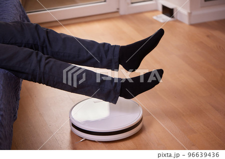 Robotic vacuum cleaner cleaning the room while man sitting on sofa. Robotic vacuum cleaner cleaning the room while man sitting on sofa. 96639436