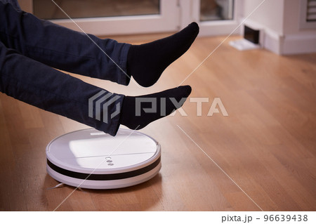Robotic vacuum cleaner cleaning the room while man sitting on sofa. Robotic vacuum cleaner cleaning the room while man sitting on sofa. 96639438