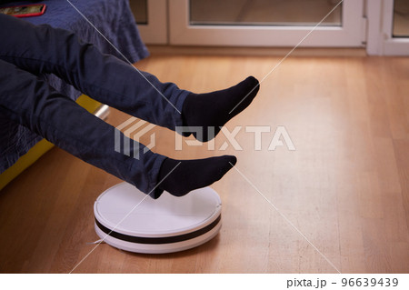 Robotic vacuum cleaner cleaning the room while man sitting on sofa. Robotic vacuum cleaner cleaning the room while man sitting on sofa. 96639439