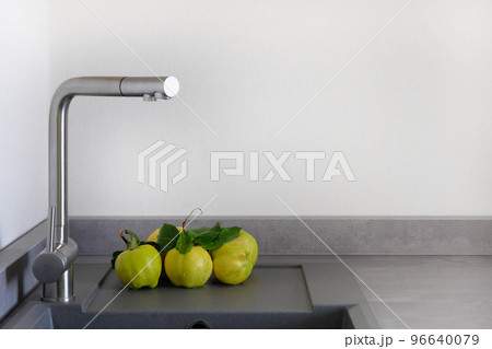 Yellow juicy apple quince next to sink in kitchen room. Modern counter with sink in kitchen room. Washing vegetables concept. Copy space. Yellow juicy apple quince next to sink in kitchen room. Modern counter with sink in kitchen room. Washing vegetables concept. Copy space. 96640079