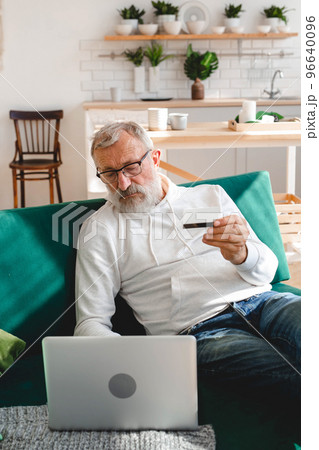 Senior elderly man making online payments using laptop. Old grandfather doing shopping ecommerce with credit card. Pensioner holding debit card for internet banking. Copy space and place advertising 96640096