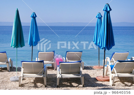 Blue umbrellas and chaise for relax on sea coast. Happy summer vacations and travel concept. Paid service on beaches. Blue umbrellas and chaise for relax on sea coast. Happy summer vacations and travel concept. Paid service on beaches. 96640356