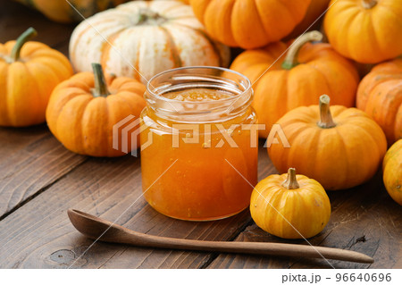Jar of healthy pumpkin jam and wooden spoon. Pumpkins on kitchen table. 96640696