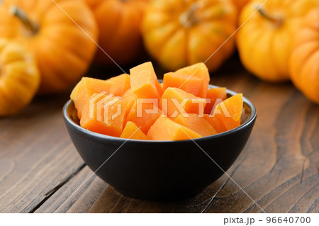 Bowl of chopped pumpkin pulp on kitchen table. Pumpkins in background. 96640700