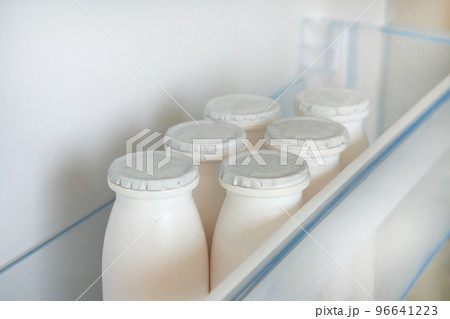 White bottles of kefir on shelf of open empty refrigerator. Fermented food concept. White bottles of kefir on shelf of open empty refrigerator. Fermented food concept. 96641223