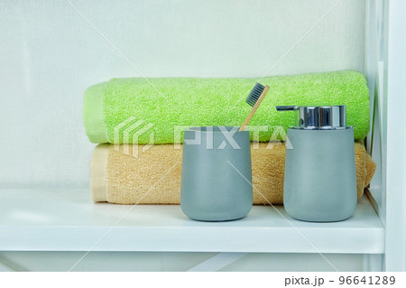 Light gray ceramic acessories for bath - soap dispenser, wooden toothbrush and towels for personal hygiene. Decor for bathroom interior. 96641289