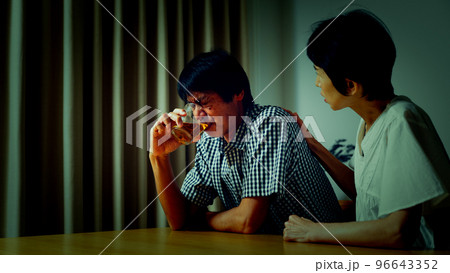 家でうなだれるミドル男性と彼を慰めるミドル女性	 96643352