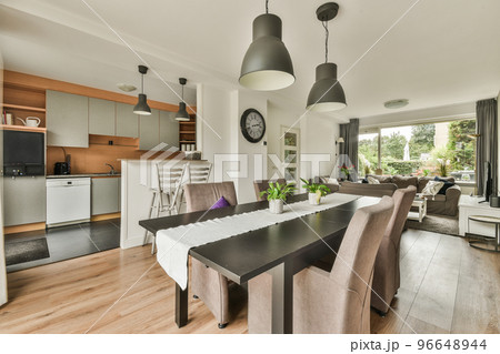 Table with chairs and flowers located near lounge area and kitchen in spacious room of contemporary apartment 96648944