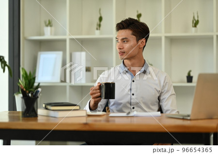 Thoughtful millennial businessman drinking coffee and and looking through a window, thinking or visualizing career success Thoughtful millennial businessman drinking coffee and and looking through a window, thinking or visualizing career success 96654365