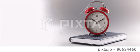 Red retro clock stand on top of closed book or diary, time to study, time to learn new information Red retro clock stand on top of closed book or diary, time to study, time to learn new information 96654460