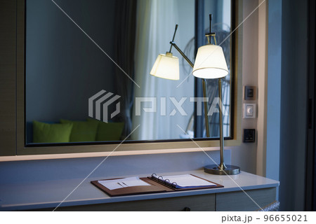 The desk in the room had a lamp on the table. There is a mirror on the back. 96655021