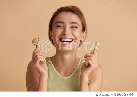 Face massage. Laughing Woman Posing With Jade Facial Roller for Skin Care Face massage. Laughing Woman Posing With Jade Facial Roller for Skin Care 96655744