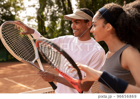 Young male coach teaching a curly-haired girl to play tennis 96656869