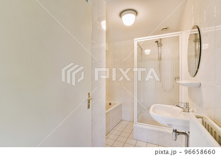 Sinks with mirrors and clean bathtub located near shower box with glass door in modern bathroom with white tiled walls Sinks with mirrors and clean bathtub located near shower box with glass door in modern bathroom with white tiled walls 96658660