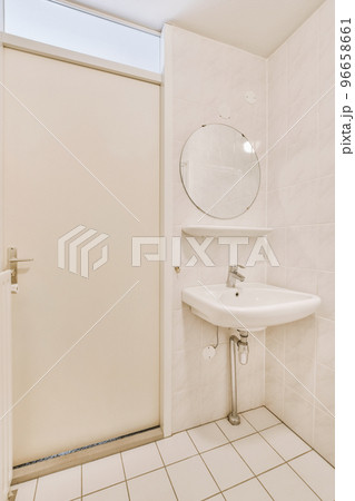 Cupboard with sink and mirror attached to tiled wall near door and drying rack in modern restroom Cupboard with sink and mirror attached to tiled wall near door and drying rack in modern restroom 96658661