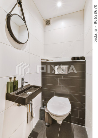 Interior of narrow restroom with sink and wall hung toilet with white walls and checkered floor 96658670