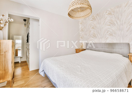 Home interior design of bedroom with bed and wooden wardrobe placed in corner near window in modern apartment 96658671