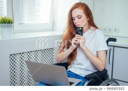Confident happy redhaired ginger businesswoman student in wheelchair doing online shopping with credit card at office Confident happy redhaired ginger businesswoman student in wheelchair doing online shopping with credit card at office 96660382