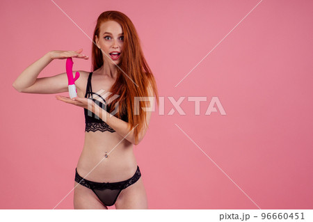 sex education concept.beautiful amazed and surprised redhaired ginger woman in sexy black linen lace holding vibro dildo in studio pink background sex education concept.beautiful amazed and surprised redhaired ginger woman in sexy black linen lace holding vibro dildo in studio pink background 96660451