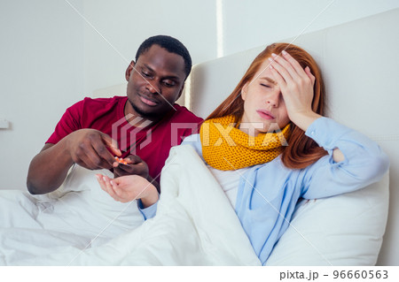 Sick together. Young latin hispanic man and redhaired ginger woman sneezing into paper napkins in bed 96660563